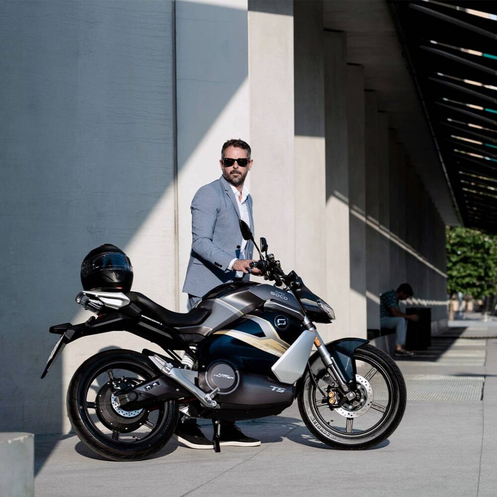 Super Soco TS Streethunter Elektromotorrad in Seitenansicht auf Parkplatz in der Stadt mit Mann